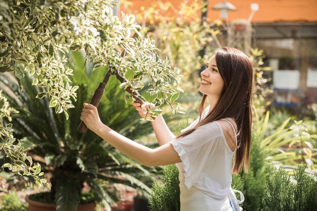 Souriante jeune femme coupe les feuilles avec des ciseaux de jardinage