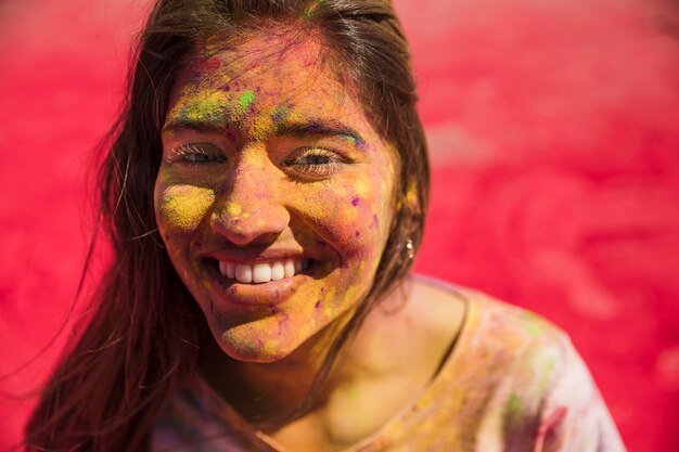 Souriante jeune femme a couvert son visage avec la couleur holi en regardant la caméra