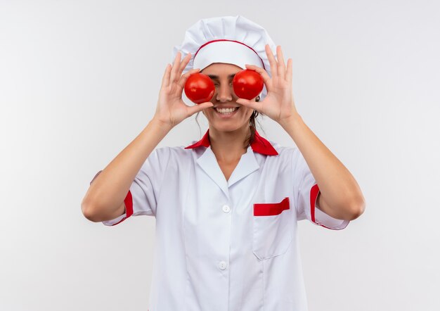 Souriante jeune femme cuisinier portant l'uniforme de chef couvert de tomates avec espace copie