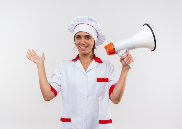 Souriante jeune femme cuisinier portant l'uniforme de chef tenant la main de haut-parleur avec espace copie