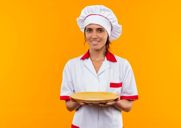 Souriante jeune femme cuisinier portant un uniforme de chef tenant la plaque avec espace copie