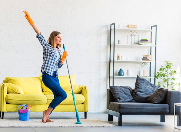 Souriante jeune femme dansant dans le salon avec des équipements de nettoyage