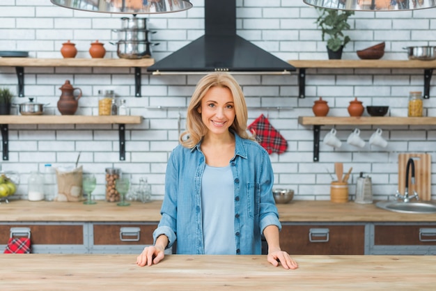 Souriante jeune femme debout derrière la table en bois dans la cuisine