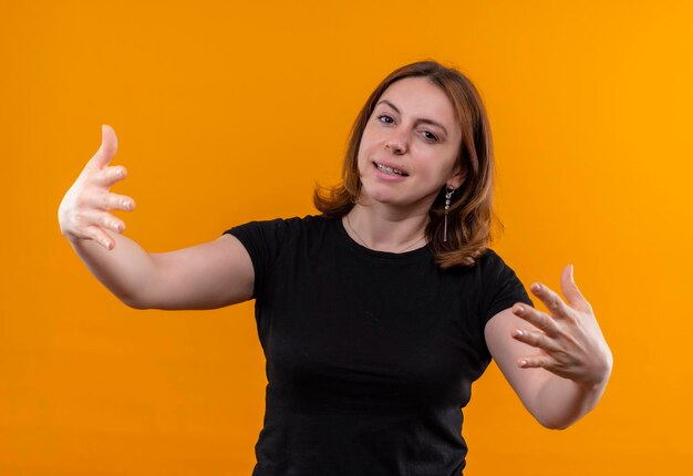 Souriante jeune femme décontractée à bras ouverts sur l'espace orange isolé