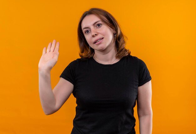 Souriante jeune femme décontractée faisant des gestes salut sur l'espace orange isolé