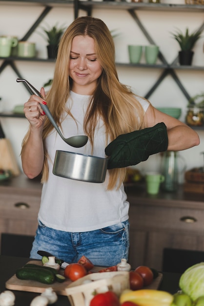 Souriante jeune femme dégustant des aliments debout derrière le comptoir de la cuisine