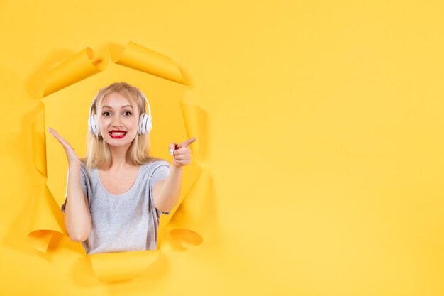 Souriante jeune femme écoutant de la musique dans des écouteurs sur fond jaune échographie sonore audio