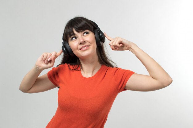 Souriante jeune femme écoutant de la musique à travers des écouteurs en t-shirt conçu de bonne humeur avec des cheveux longs sur blanc