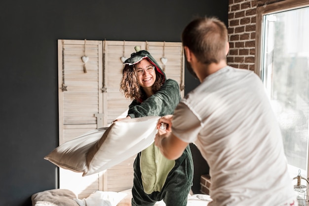 Photo gratuite souriante jeune femme faisant la bataille d'oreillers avec son mari à la maison