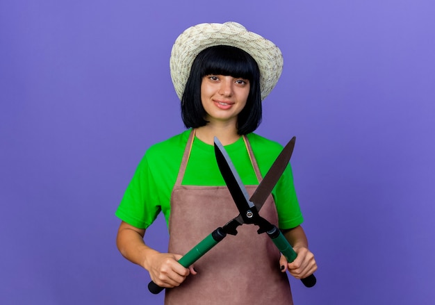 Souriante jeune femme jardinière en uniforme portant chapeau de jardinage détient tondeuses à la recherche
