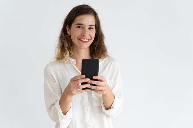 Souriante jeune femme jolie navigation sur smartphone et en regardant la caméra.