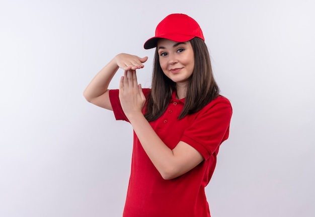 Souriante jeune femme de livraison portant un t-shirt rouge en bonnet rouge montrant le délai d'attente sur un mur blanc isolé