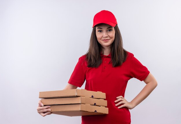 Souriante jeune femme de livraison portant un t-shirt rouge en bonnet rouge tenant une boîte à pizza sur un mur blanc isolé