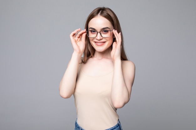 Souriante jeune femme avec des lunettes sur mur gris