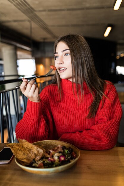 Souriante jeune femme mangeant de la salade fraîche au restaurant