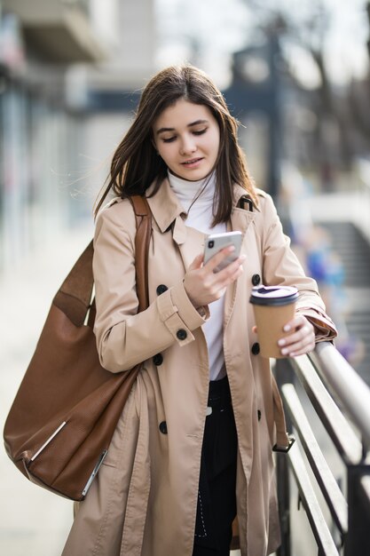 Souriante jeune femme en manteau marron clair dans la ville