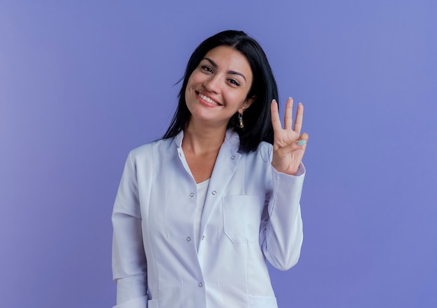 Souriante jeune femme médecin portant une robe médicale à la recherche de trois avec la main