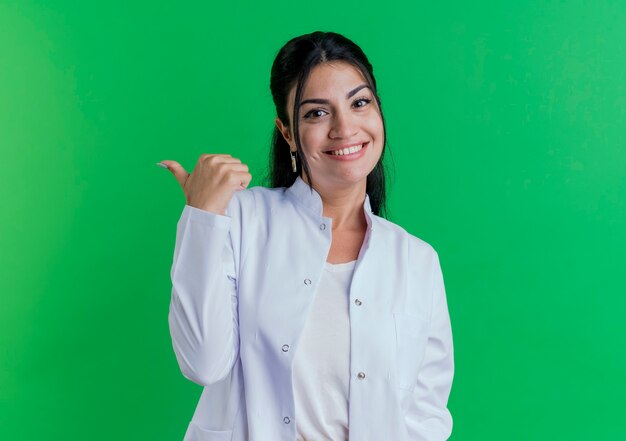 Souriante jeune femme médecin portant une robe médicale regardant pointant sur le côté