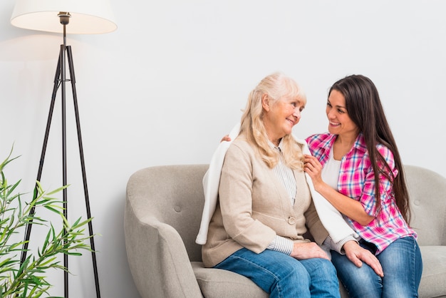 Souriante jeune femme mettant une couverture sur l&#39;épaule de mère senior