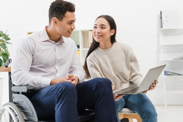 Souriante jeune femme montrant quelque chose à un homme d&#39;affaires assis sur un fauteuil roulant