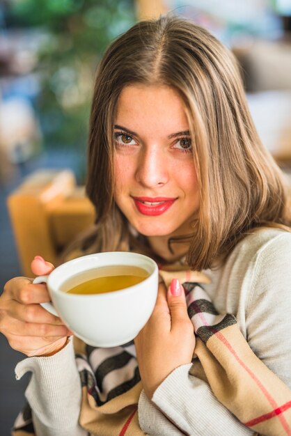 Souriante jeune femme montrant une tisane dans une tasse blanche