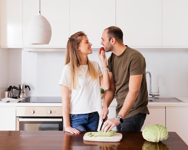 Souriante jeune femme nourrit sa salade à son mari dans la cuisine