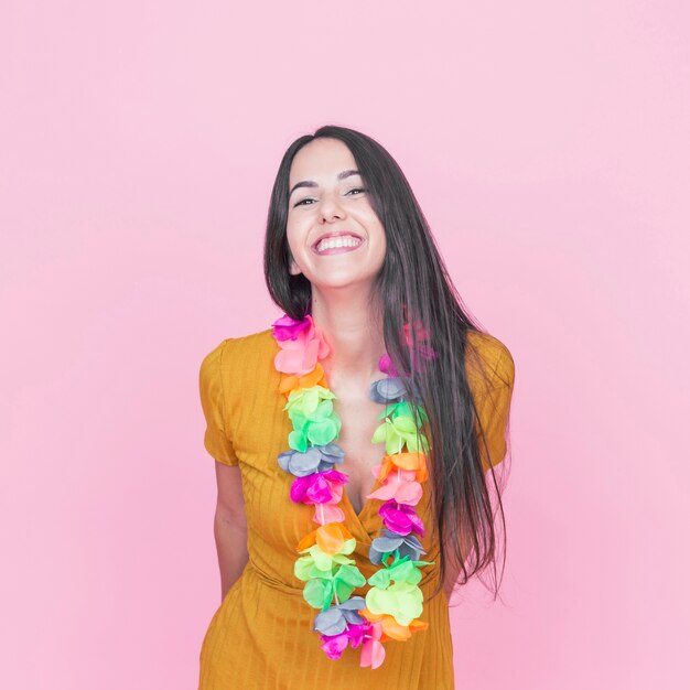 Souriante jeune femme portant une guirlande colorée autour de son cou sur fond rose