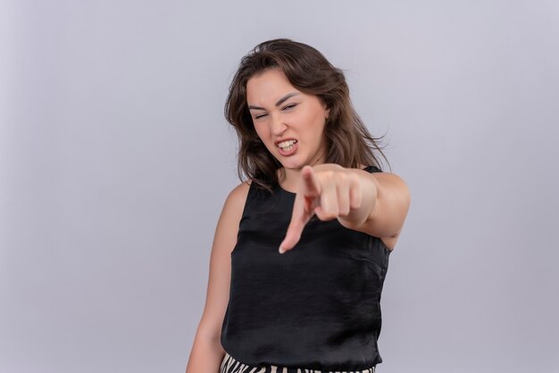 Souriante jeune femme portant un maillot noir vous montrant le geste sur le mur blanc