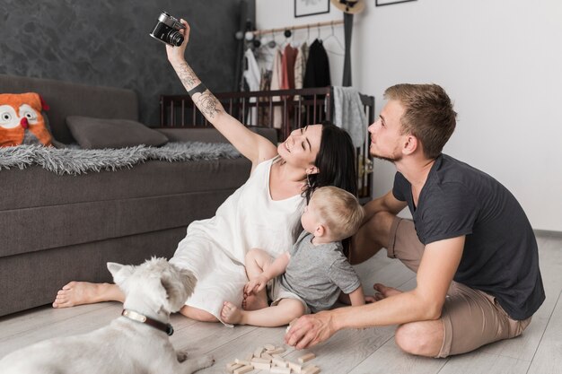 Souriante jeune femme prenant selfie de sa famille assise dans le salon