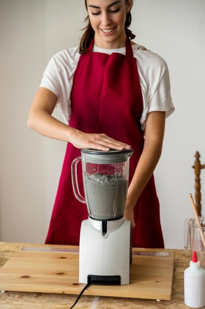 Souriante jeune femme prépare la pâte à papier dans un mélangeur