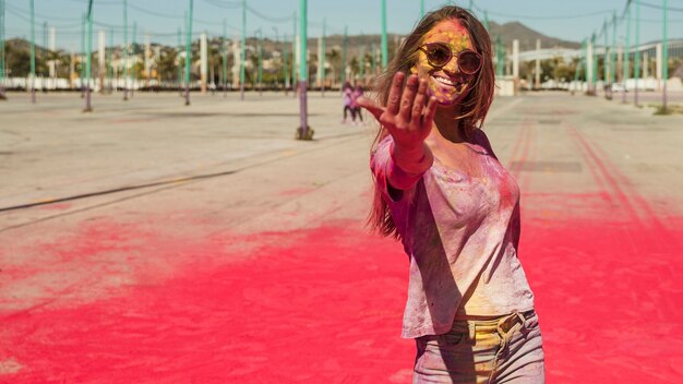 Souriante jeune femme recouverte de couleur holi appelant devant la caméra