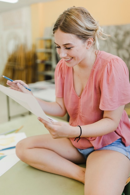 Photo gratuite souriante jeune femme regardant du papier toile en atelier