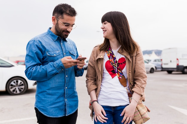 Photo gratuite souriante jeune femme regardant l'homme à l'aide de téléphone portable à la rue