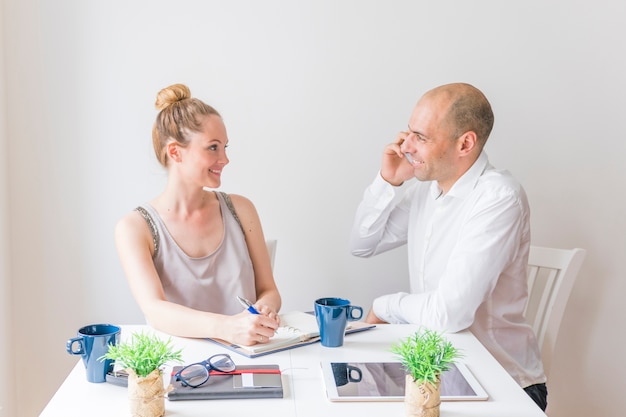 Photo gratuite souriante jeune femme regardant un homme parlant au téléphone portable au lieu de travail