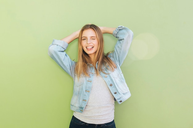 Souriante Jeune Femme Avec Ses Mains Derrière La Tête, Clignant De L'oeil Contre La Toile De Fond Verte