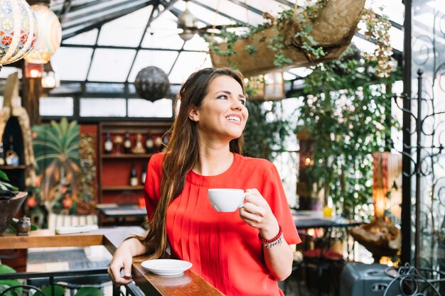 Souriante jeune femme avec une tasse de café au café