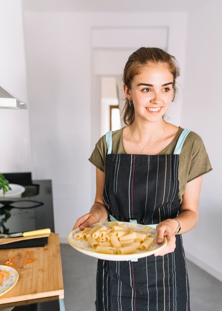 Souriante jeune femme tenant l&#39;assiette de pâtes rigatoni dans la cuisine