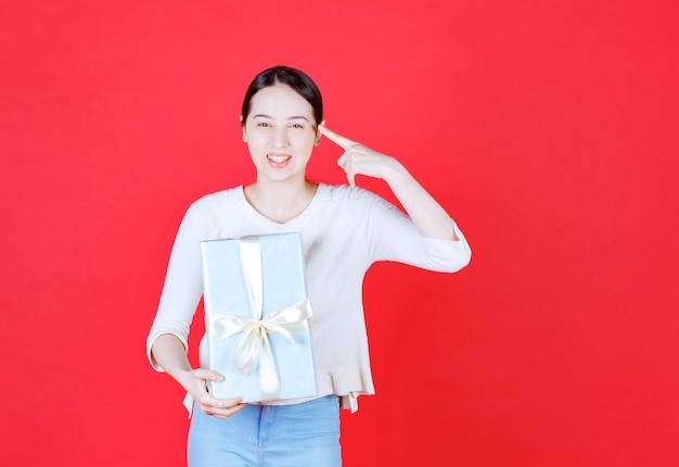 Souriante jeune femme tenant une boîte-cadeau et pointant le doigt vers sa tête