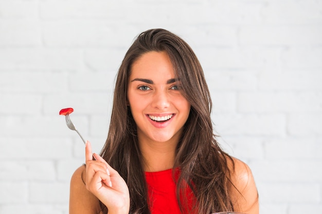 Souriante jeune femme tenant une fourchette avec une tranche de fraise