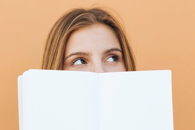 Souriante jeune femme tenant un livre blanc dans sa main en regardant la caméra