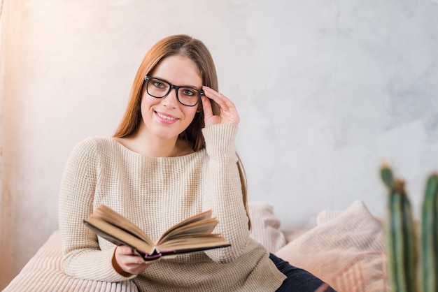 Souriante jeune femme tenant un livre à la main, assise contre le mur