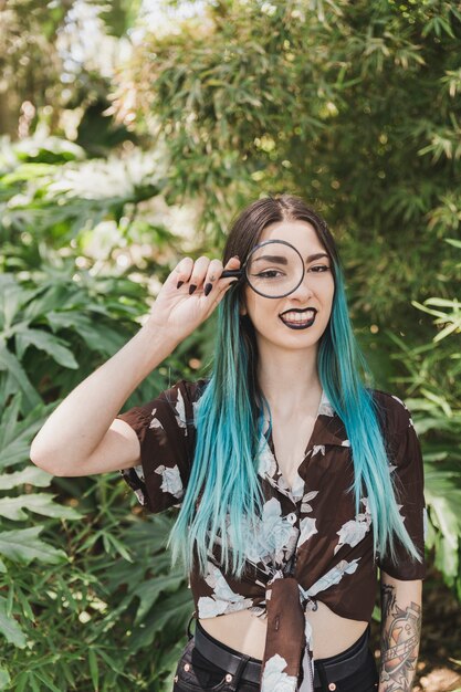 Souriante jeune femme tenant une loupe sur ses yeux