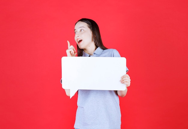 Souriante Jeune Femme Tenant Une Planche Et Pointer Le Doigt Vers Le Haut