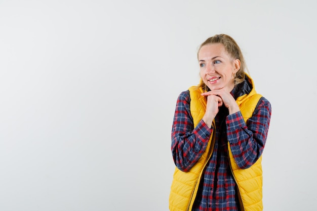 Souriante jeune femme tenant ses mains sous son menton sur fond blanc