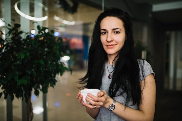 Souriante jeune femme tenant une tasse de boisson