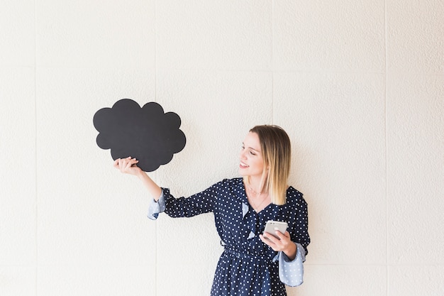 Photo gratuite souriante jeune femme tenant un téléphone mobile et nuage en carton