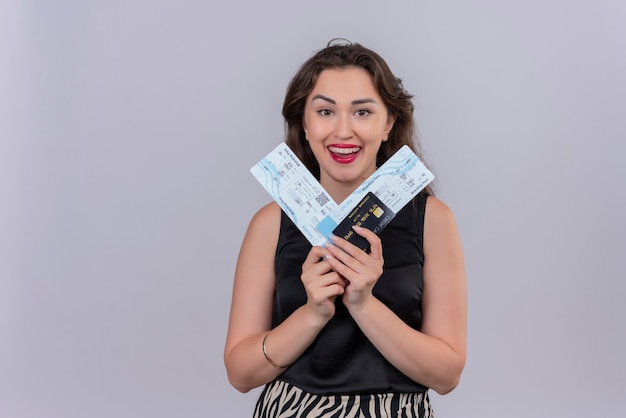 Photo gratuite souriante jeune femme voyageur portant maillot noir tenant des billets et une carte de crédit sur un mur blanc