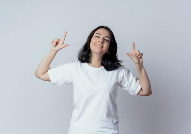 Souriante jeune fille assez caucasienne pointant avec les doigts vers le haut isolé sur fond blanc avec espace copie