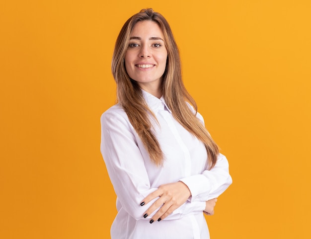 Souriante jeune fille assez caucasienne se tient avec les bras croisés isolés sur un mur orange avec espace copie