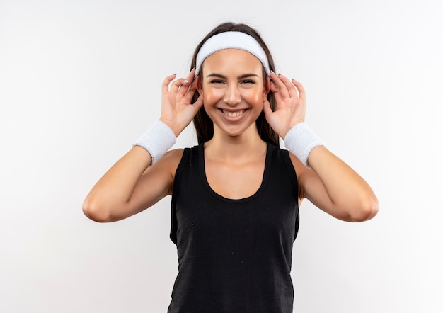 Souriante jeune fille assez sportive portant bandeau et bracelet faisant de grandes oreilles sur un espace blanc